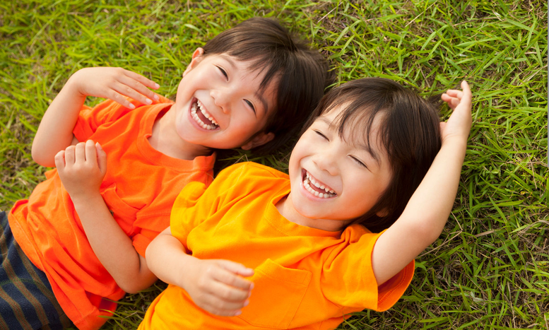 Two young siblings laughing together in the grass